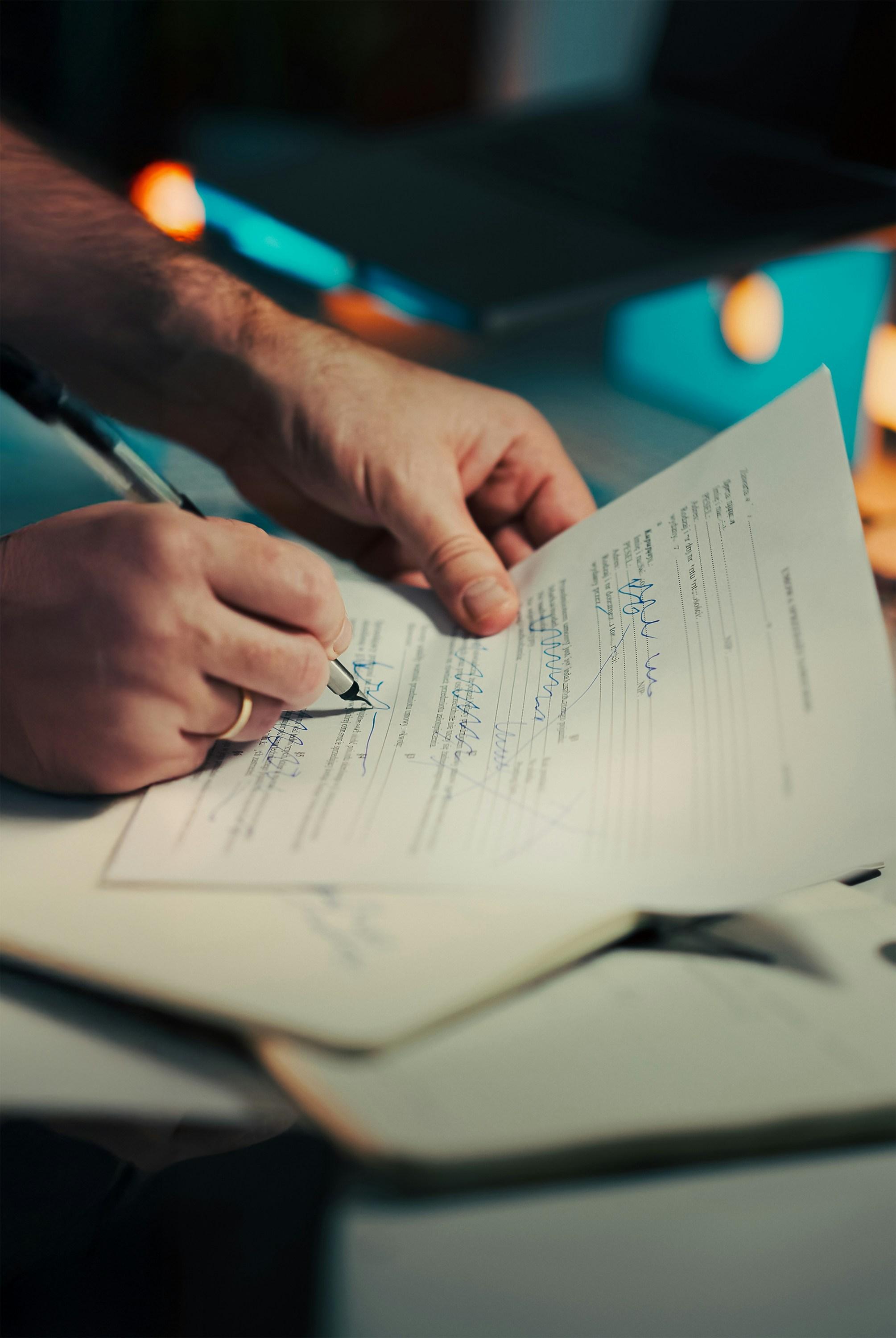 A hand signing a paper document, representing the reinstatement application filed to revive an administratively dissolved LLC.